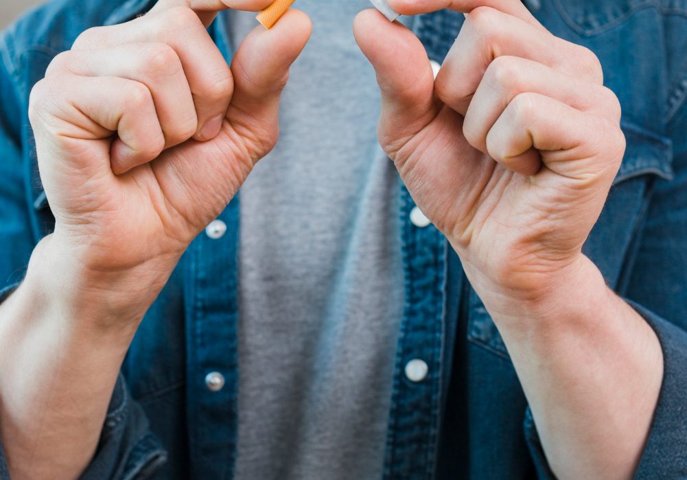 Jaunuolis su cigarete viešoje erdvėje, fone matomi draudimų ženklai – simbolizuoja griežtėjančius rūkymo ribojimus Europoje.