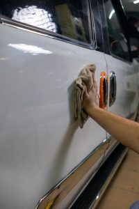 Pradedantysis poliruoja automobilio kėbulą orbitiniu poliruokliu garaže, siekdamas blizgaus paviršiaus