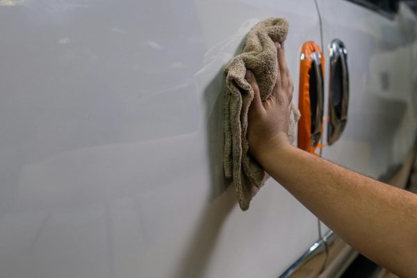 Pradedantysis poliruoja automobilio kėbulą orbitiniu poliruokliu garaže, siekdamas blizgaus paviršiaus